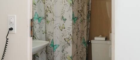 Un baño con cortina de ducha con estampado de mariposas, un inodoro y un lavabo con toma de corriente.