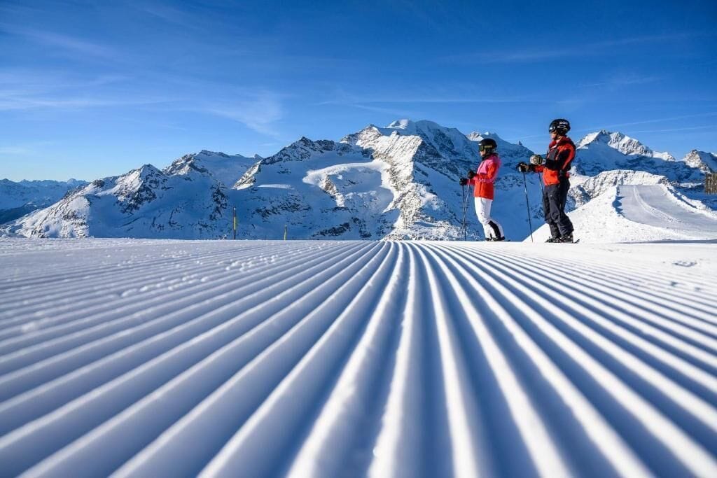 A snowy ski slope with two skiers in red jackets.