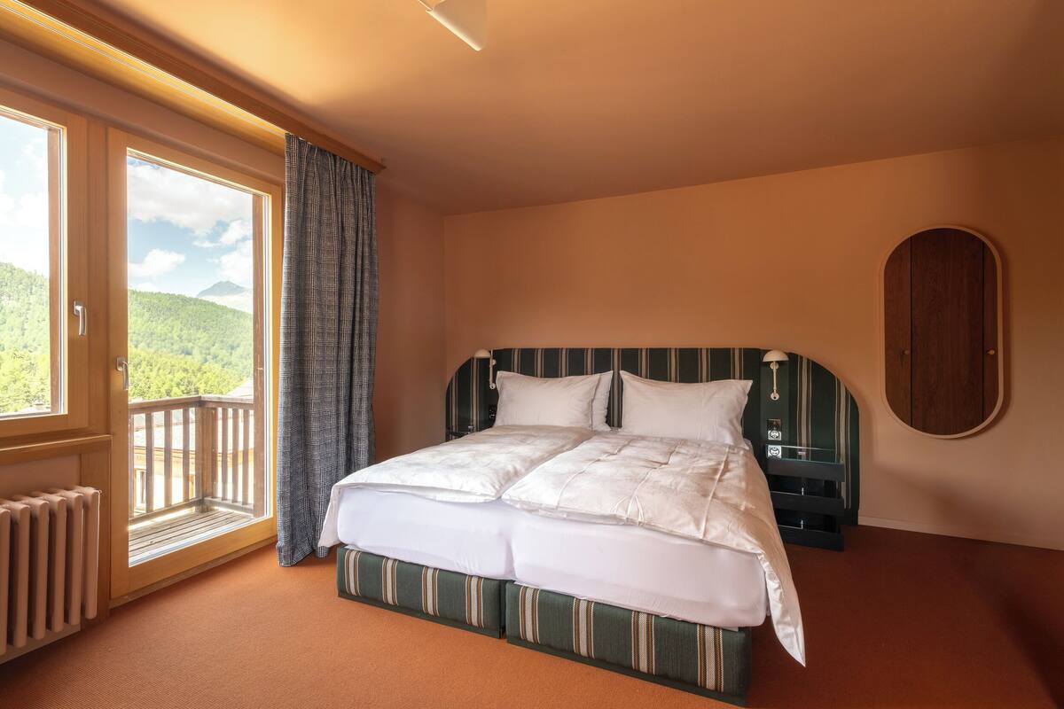 Een slaapkamer met een groot bed, een raam met uitzicht op groen en een houten hoofdbord.