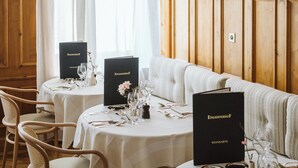A dining area with wooden paneled walls, white curtains, and tables set with fine china and glassware.