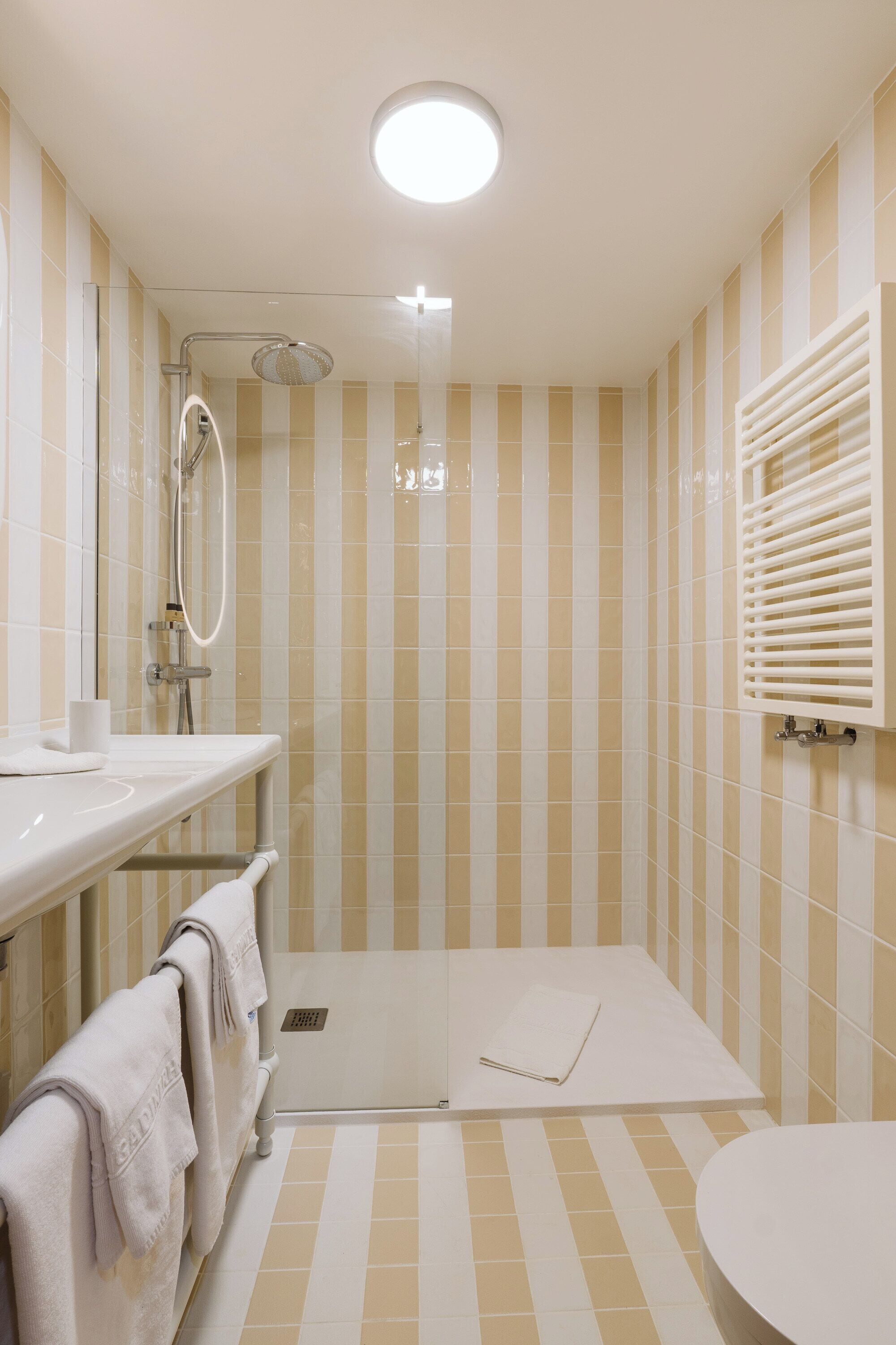 A bathroom with striped tiles, a shower, a toilet, and a towel rack.