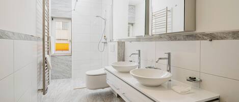 Un baño moderno con dos lavabos, ducha a ras de suelo y un espejo grande.