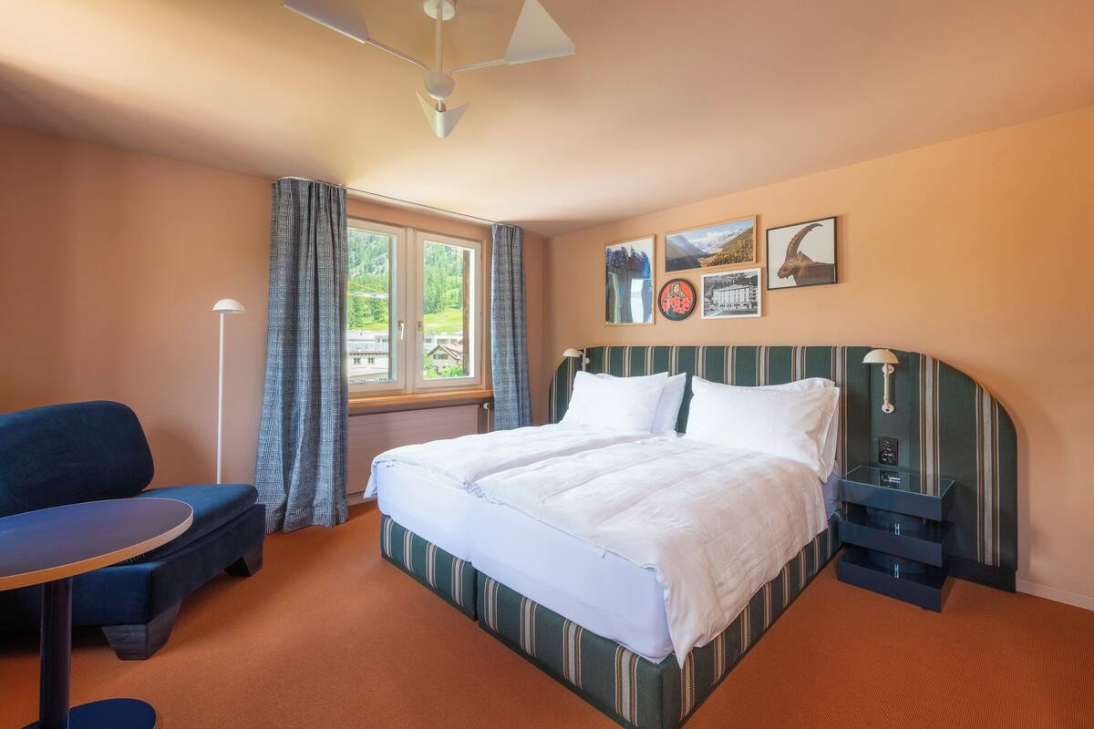 Hotelkamer met een bed, bureau, stoel, raam met gordijnen en wanddecoratie.