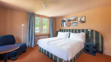 Ein Hotelzimmer mit Bett, Schreibtisch, Stuhl, einem Fenster mit Vorhängen und Wandbildern.