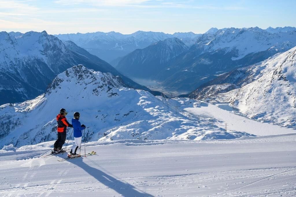 Paesaggio montuoso innevato con sciatori in una zona pianeggiante.