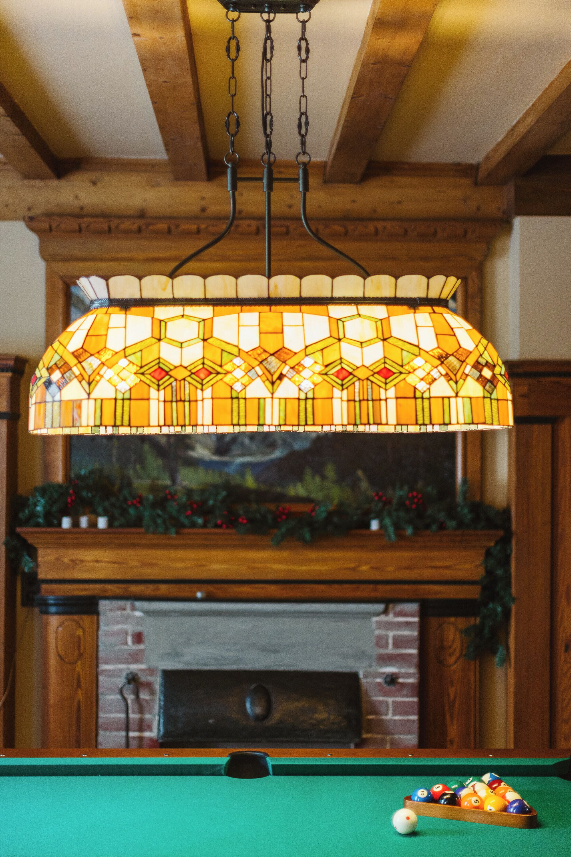 A pool table with billiard balls and a hanging stained glass light fixture above it.