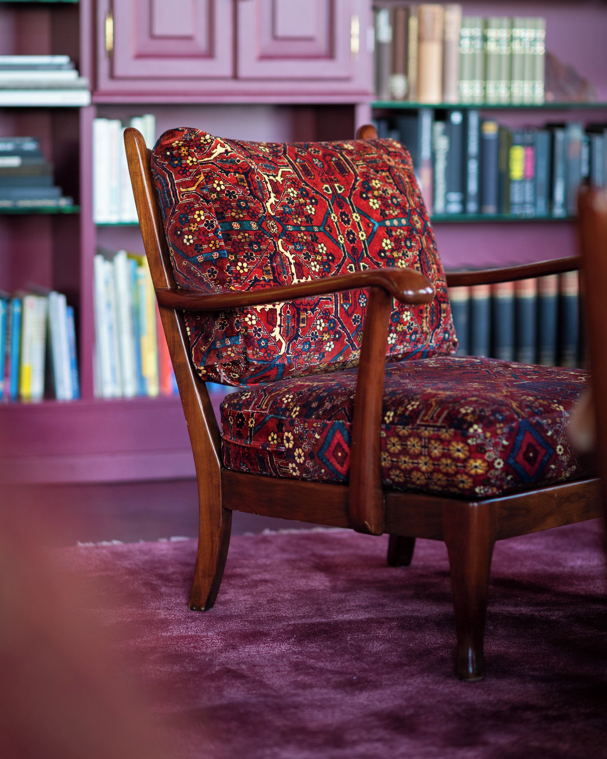 A chair with a patterned fabric, a wooden frame, and a purple carpet.