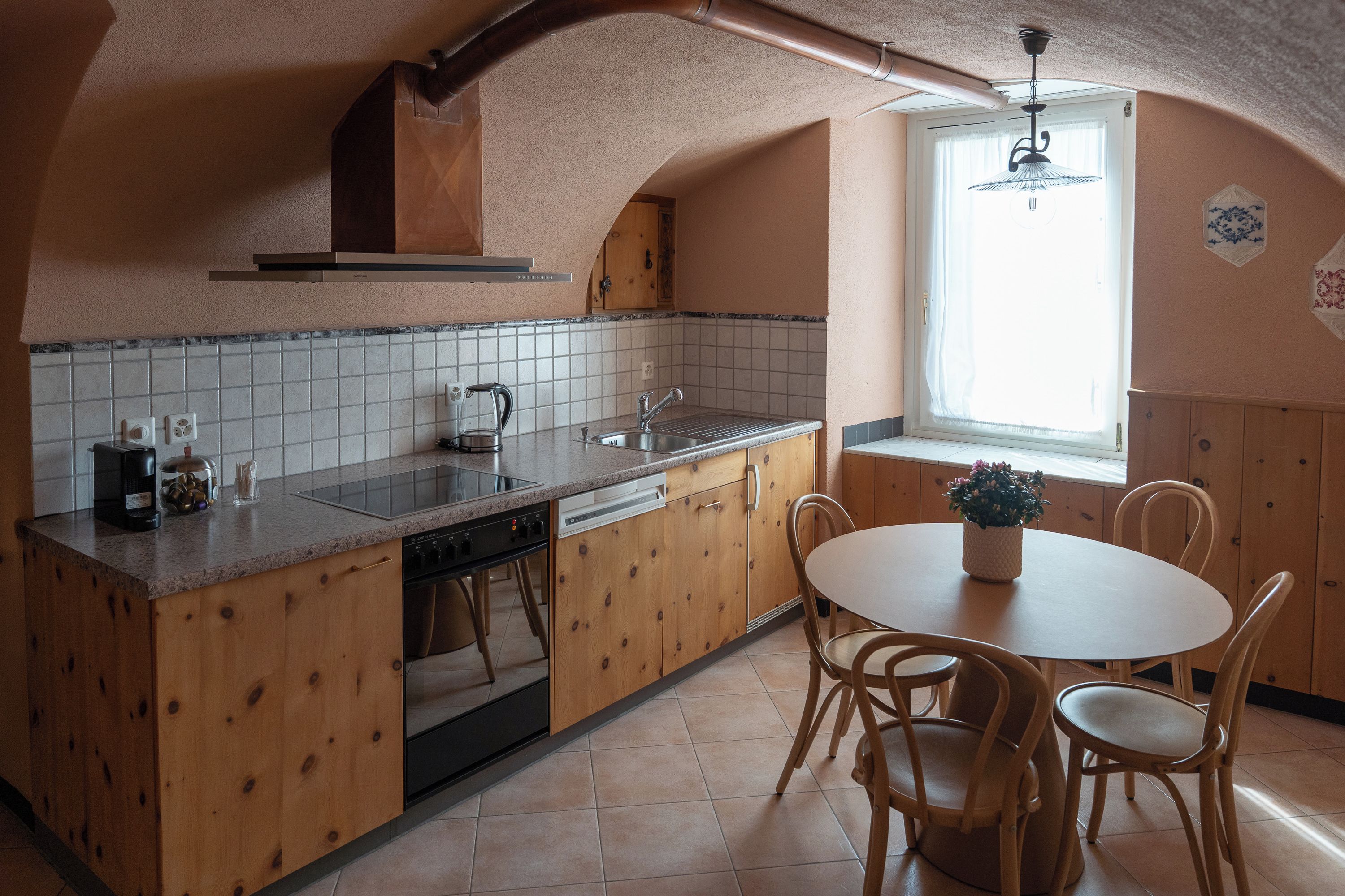 Eine Küche mit Holzausstattung, einem integrierten Geschirrspüler, einem Spülbecken und einem Fenster mit Vorhängen.