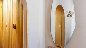 Un pasillo con un banco de madera, un espejo grande y una puerta con persianas verticales.