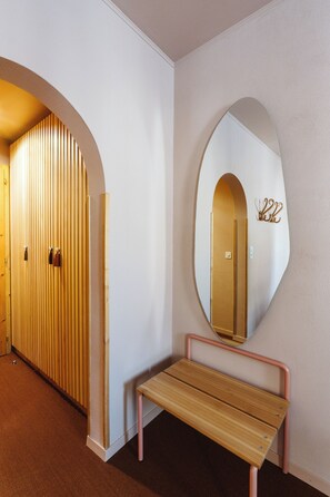 A hallway with a wooden bench, a large mirror, and a door with vertical blinds. - Boutique Hotel Engadinerhof – A Home for Generation (Pontresina)