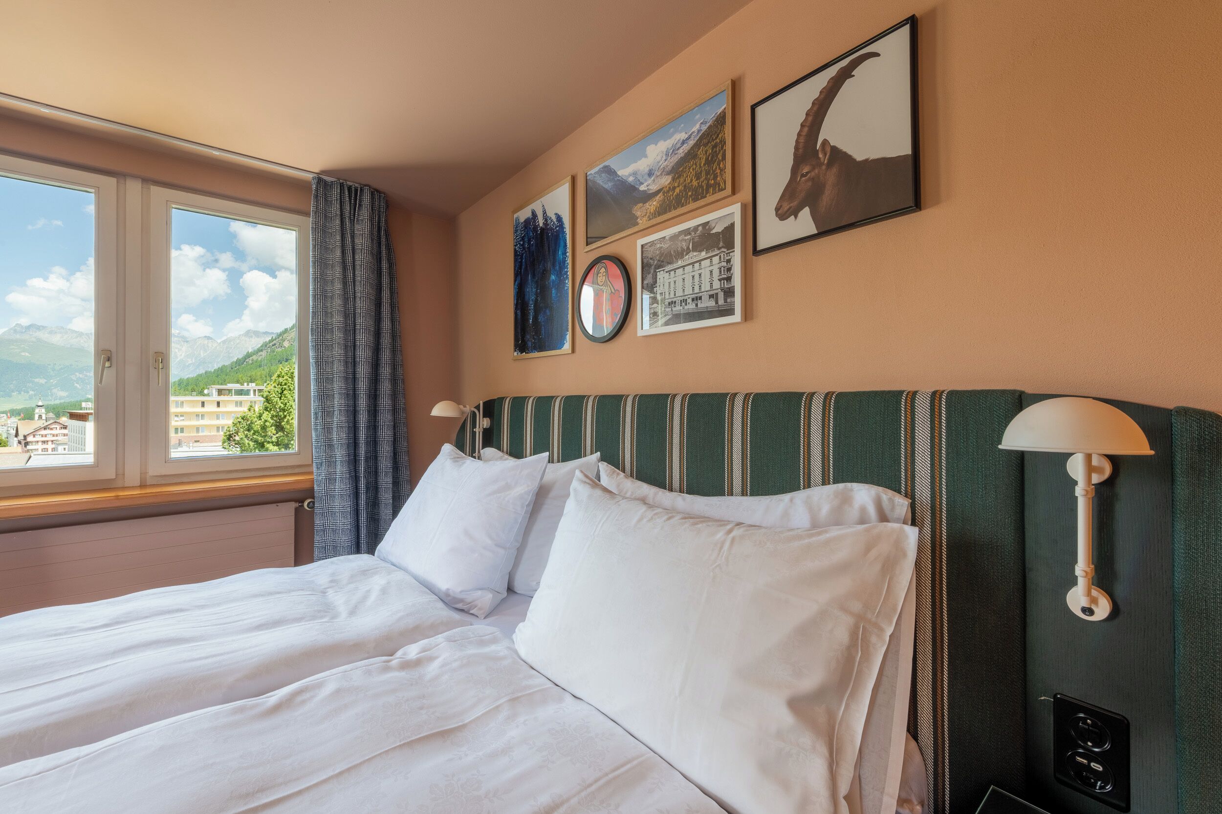A hotel room with a bed, a window with a view of mountains, and wall art.