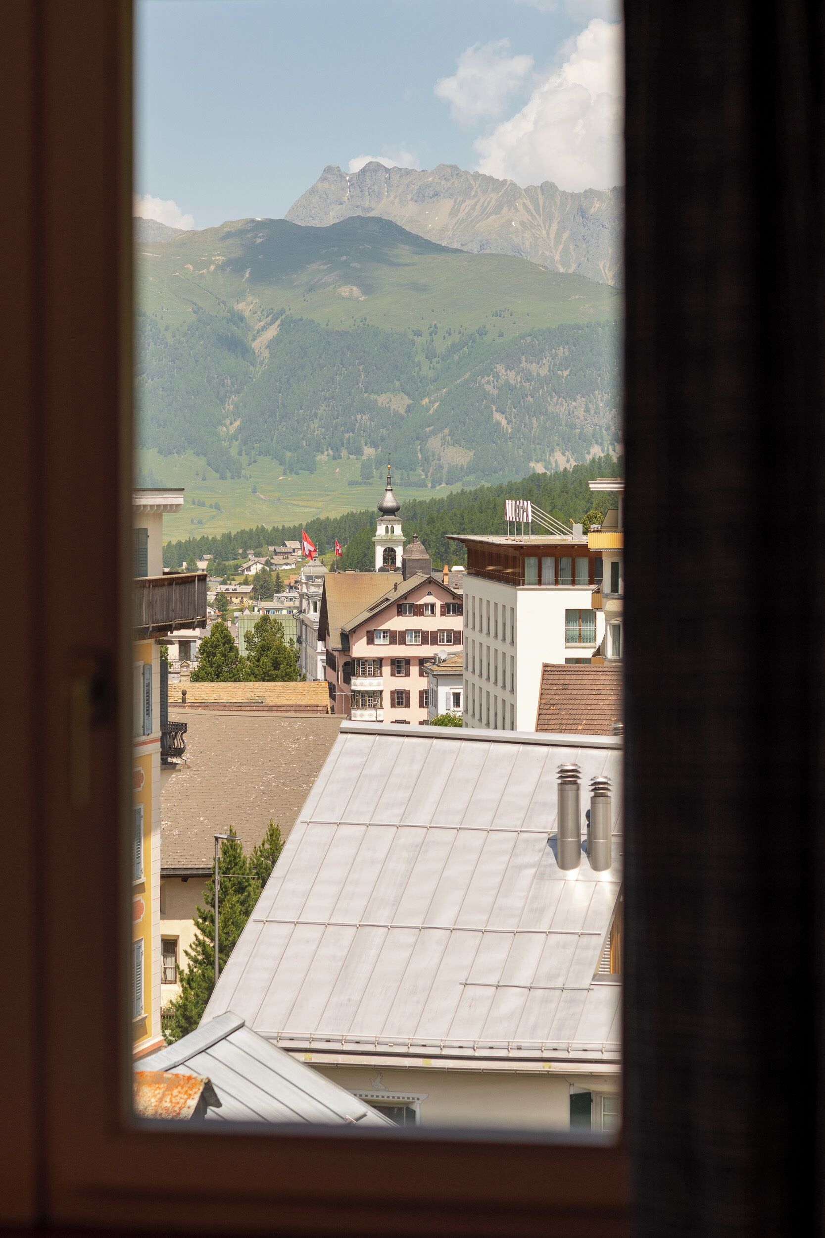 Une vue à travers une fenêtre sur une ville, avec des bâtiments et des montagnes en arrière-plan.