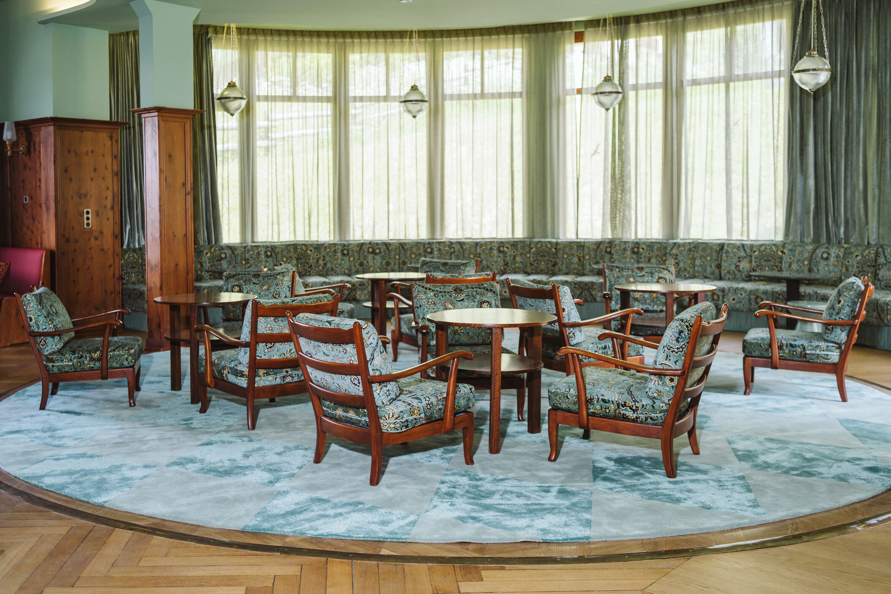 A room with a round table surrounded by chairs, a sofa, and a large window with curtains.