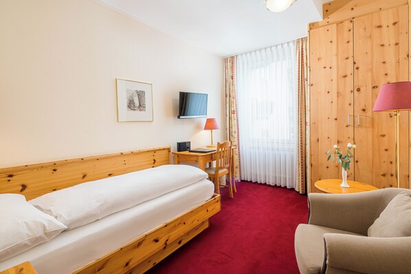 Habitación de hotel con cama de madera, un escritorio con silla, televisor y una pequeña mesa con lámpara.