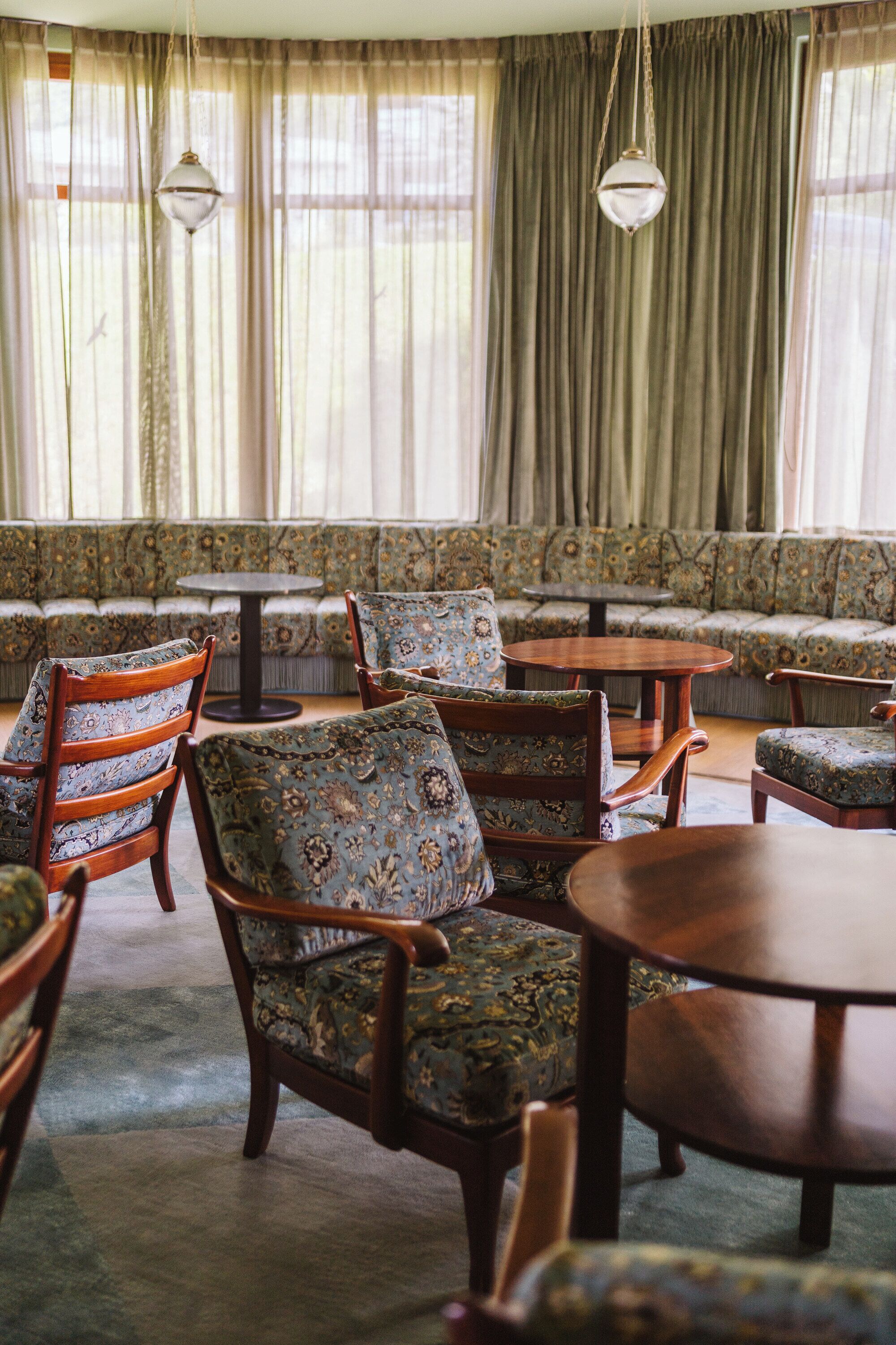 Um quarto com um sofá estofado estampado, cadeiras de madeira e uma mesa redonda.