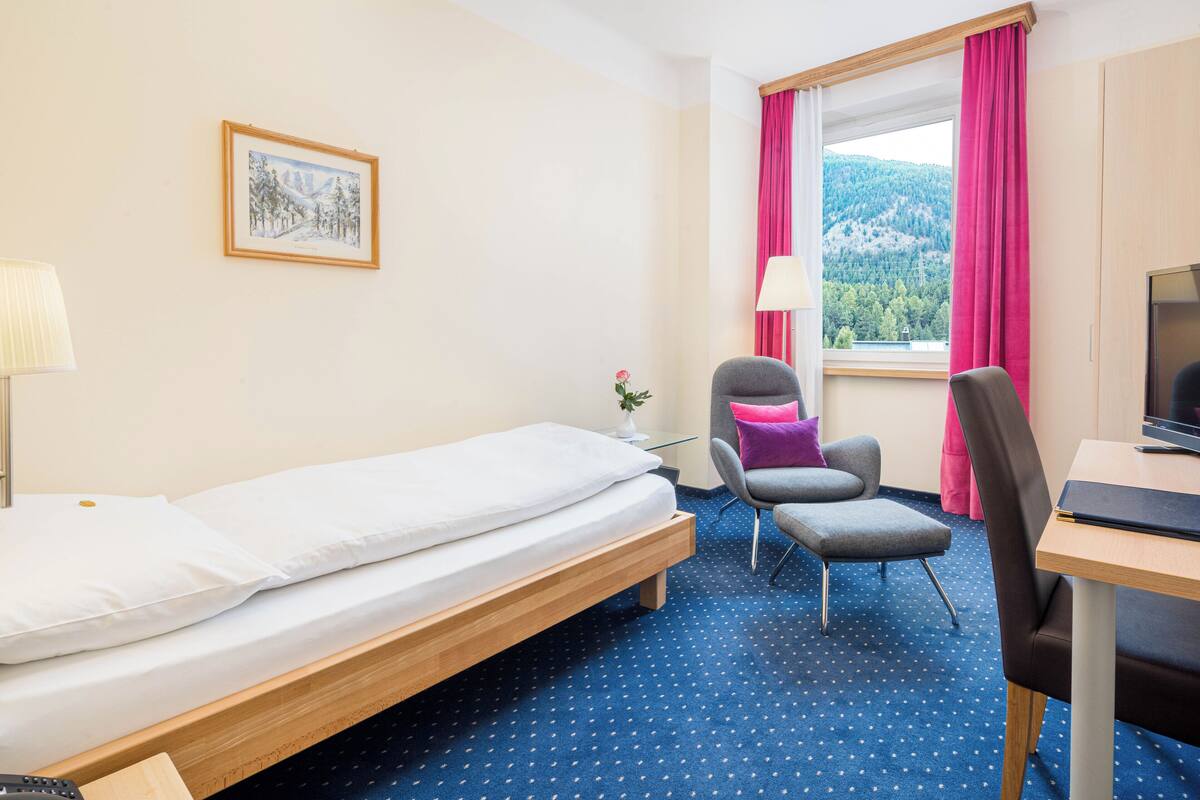 Een hotelkamer met een bed, een bureau, een stoel, een raam met gordijnen en een schilderij aan de muur.