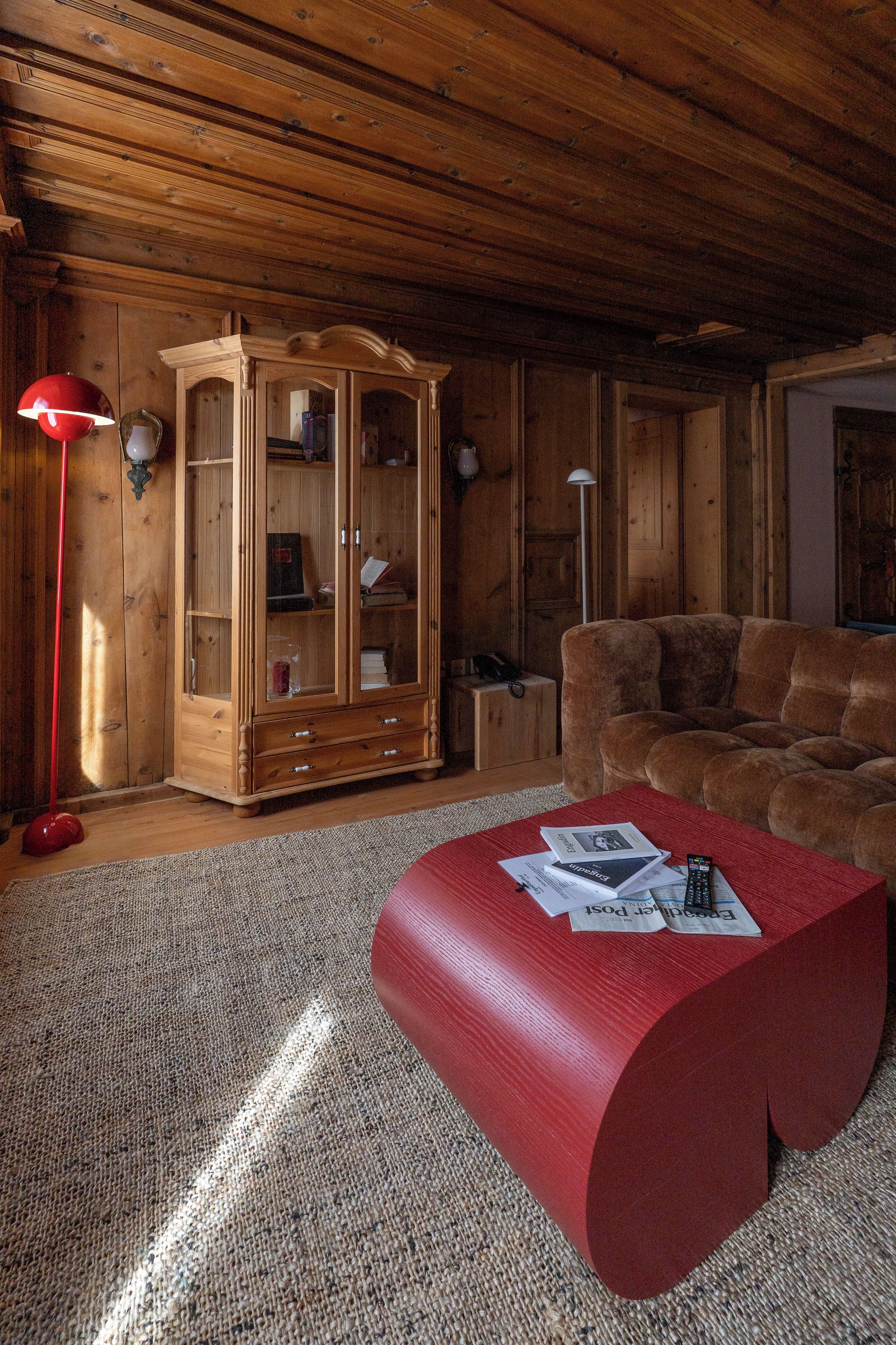 A cozy living room with a wooden cabinet, a red ottoman, and a sofa.