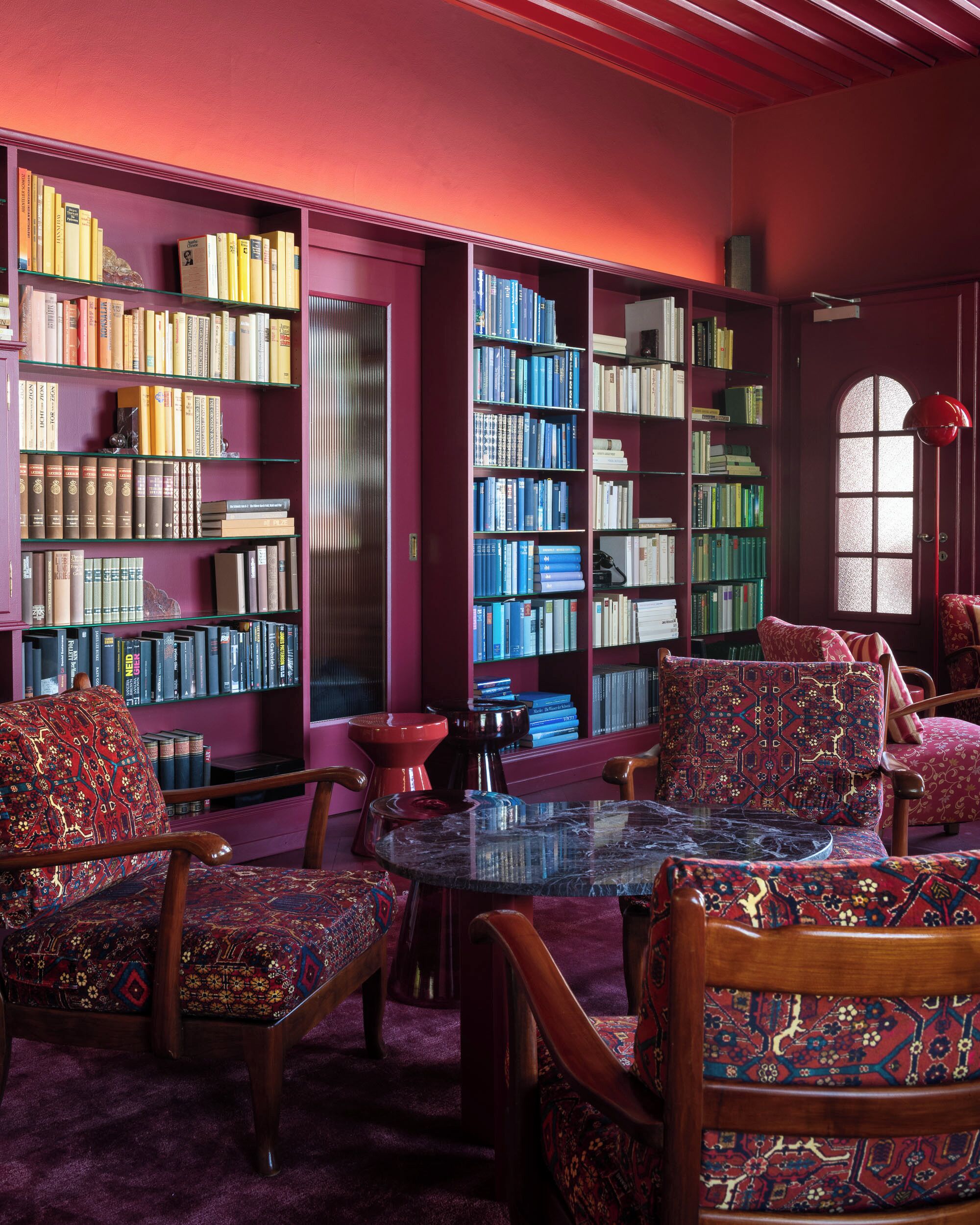 A library with bookshelves, patterned chairs, and a round table.