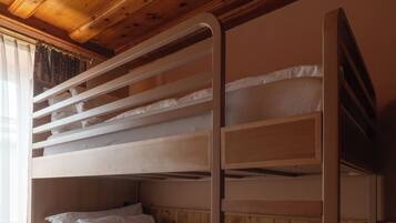Una cama litera con estructura de madera, ropa de cama blanca y una ventana con cortinas.