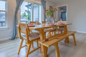 A dining area with a wooden table and chairs, a bench, a vase with flowers, and a glass on the table. - The Axelrod | Sleeps 16 (Houston)
