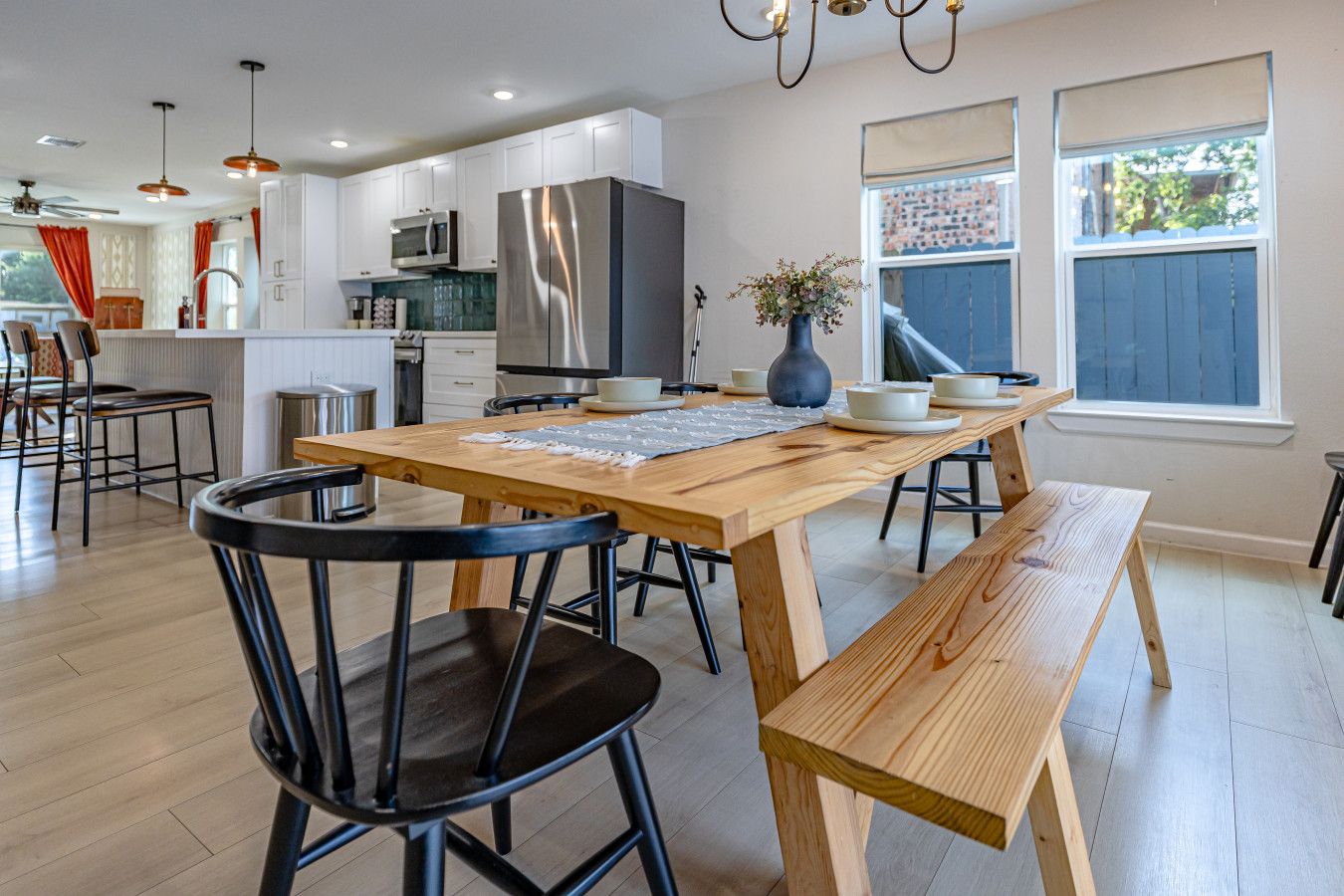 A modern kitchen with a wooden table, black chairs, and a stainless steel refrigerator.