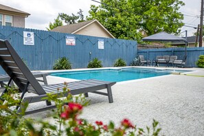 A swimming pool with lounge chairs, a blue fence, and warning signs. - The Axelrod | Sleeps 16 (Houston)