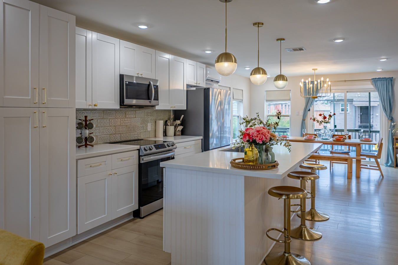 A modern kitchen with white cabinetry, stainless steel appliances, and a central island with stools.