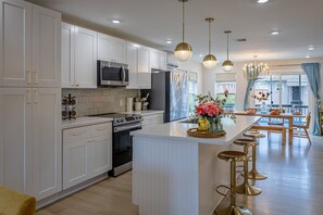 A modern kitchen with white cabinetry, stainless steel appliances, and a central island with stools.