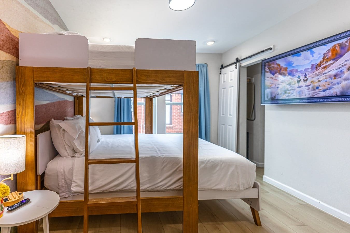 Une chambre avec des lits superposés, un téléviseur fixé au mur, une lampe et une petite table avec une télécommande.
