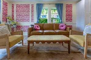 A living room with a brown leather sofa, two wooden armchairs, a wooden coffee table, and patterned wallpaper.