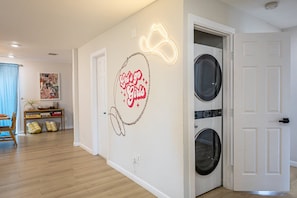 Una sala de lavandería con un letrero de neón, una lavadora y una puerta.