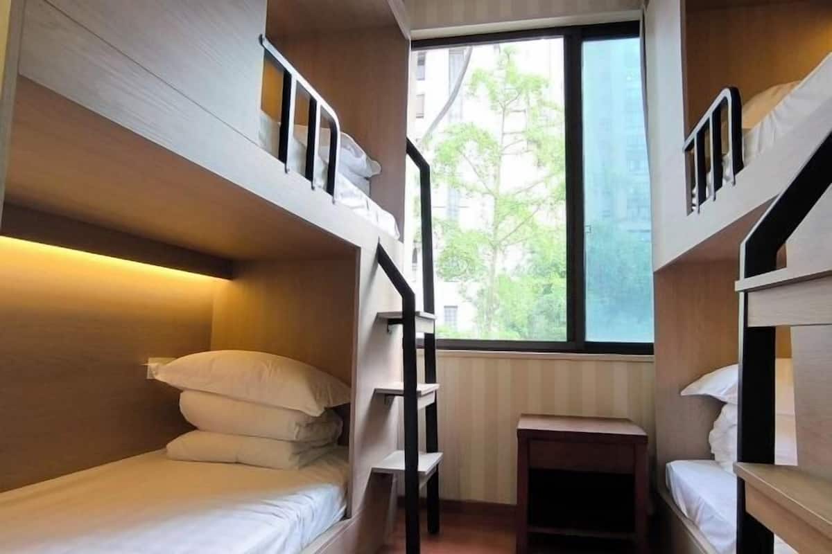A compact room with bunk beds, a small desk, and a window providing a view of the outside.