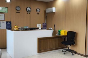 A reception desk with a computer, a telephone, and a small statue. There are clocks on the wall and a yellow sign. - Rlan Boutique Hotel (Shanghai)