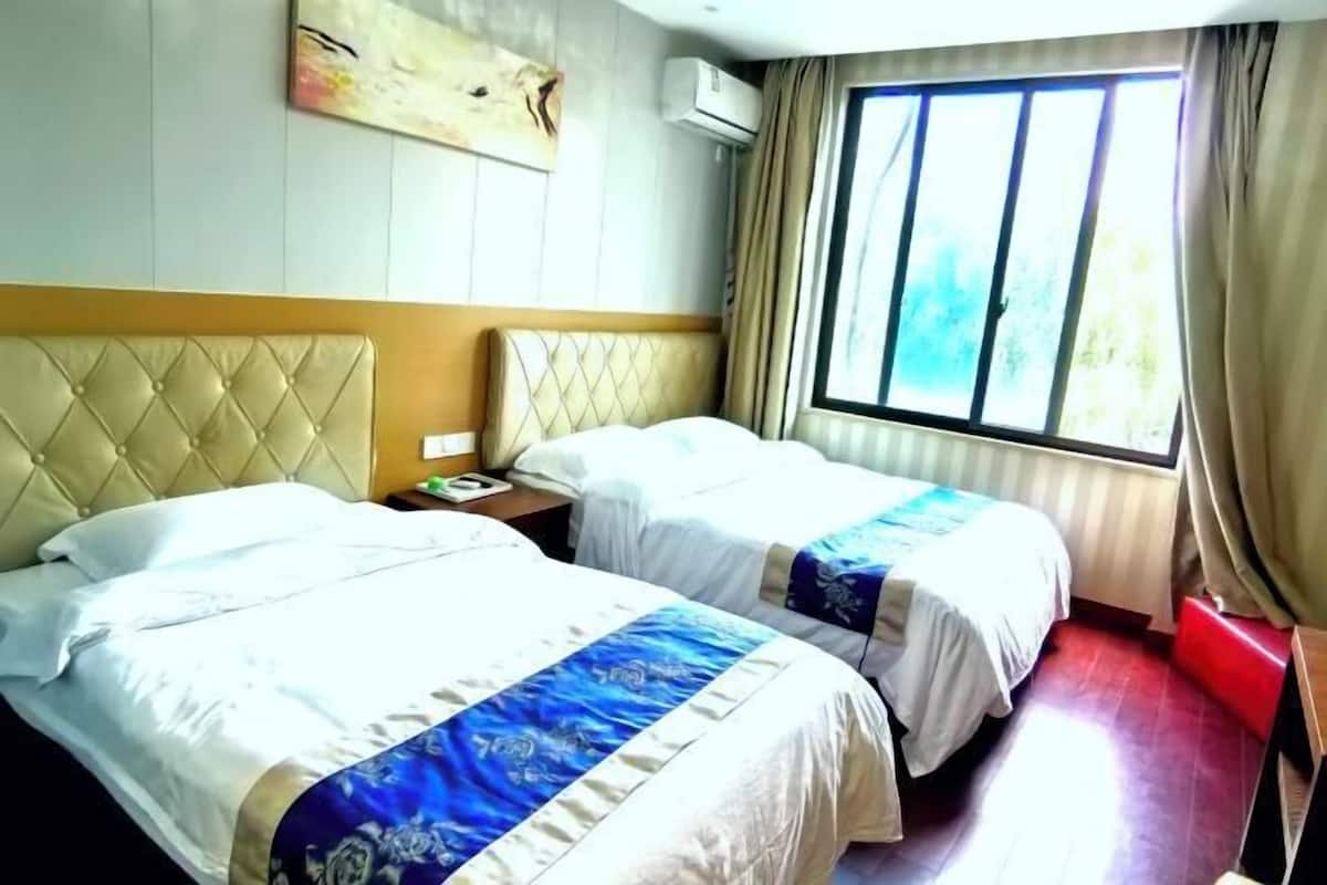 A hotel room with two beds, a large window with curtains, a wall-mounted air conditioner, and a piece of abstract art.