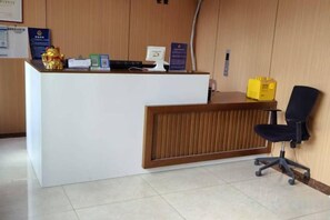 A reception desk with a computer, a telephone, and a yellow box. There is a black office chair and a wooden panel wall. - Rlan Boutique Hotel (Shanghai)