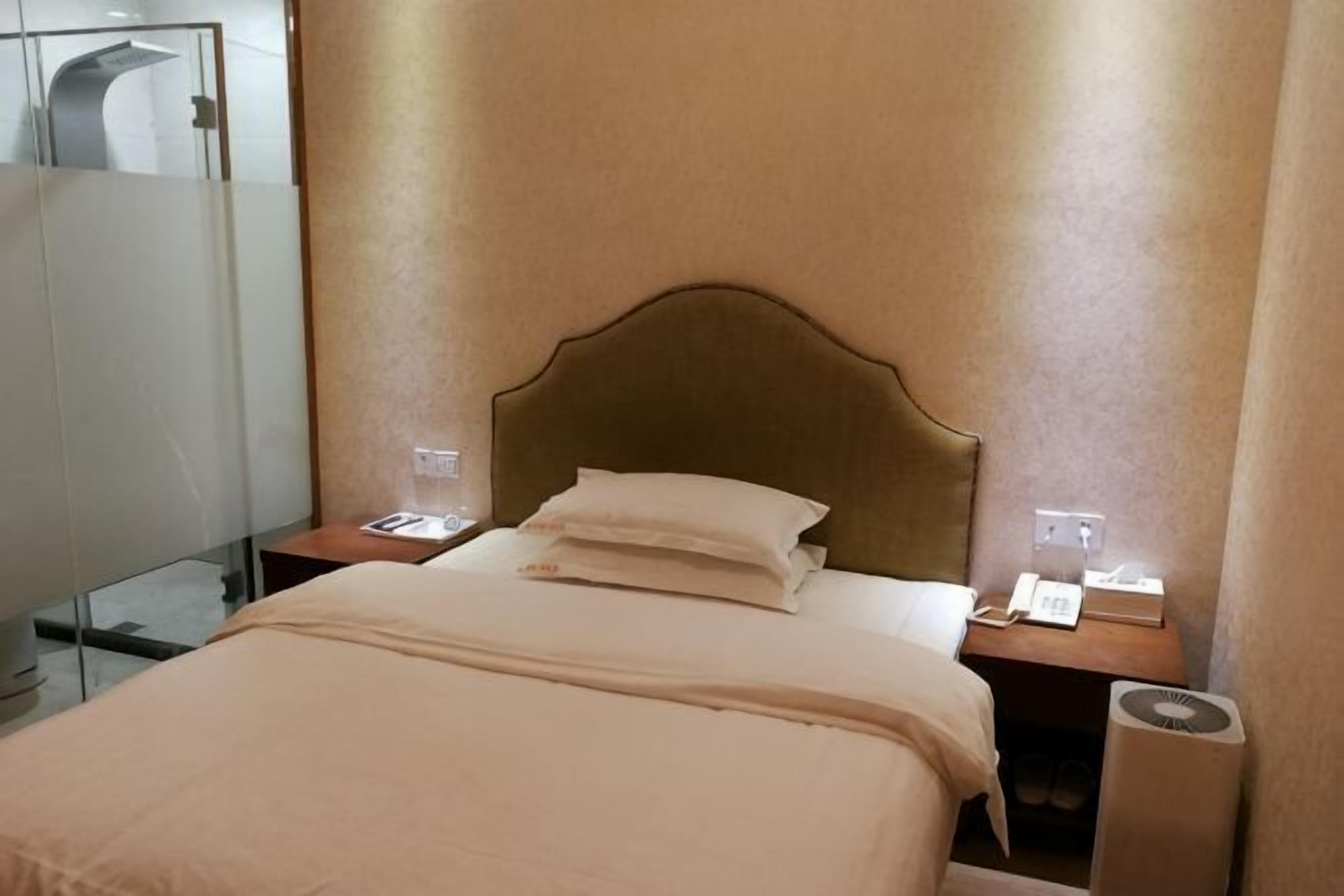 A hotel room with a bed, bedside tables, a mirror, and a wall-mounted telephone.