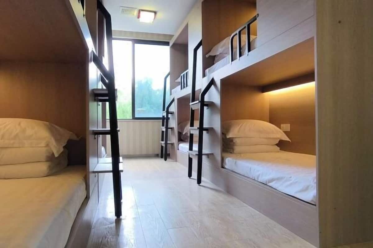 A dormitory room with bunk beds, a radiator, and a window providing natural light.