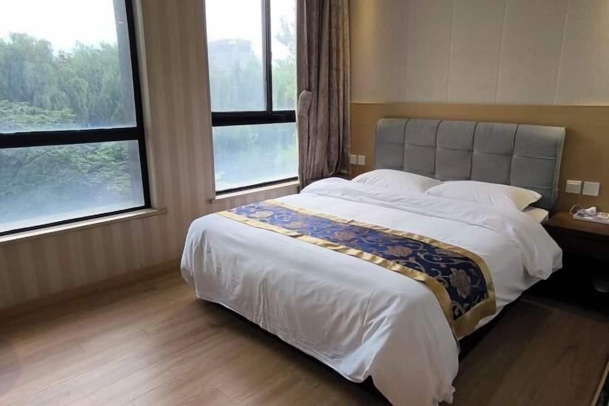 A hotel room with a large window, a bed with a patterned bedspread, and a wooden floor.