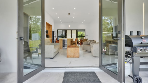 Un salon moderne doté d’une porte vitrée donnant sur un espace extérieur, d’une table basse en bois et d’un barbecue.