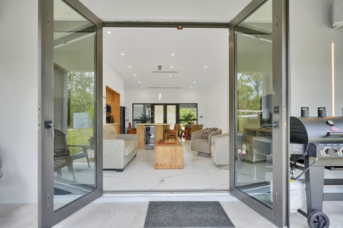 A modern living room with a glass door leading to an outdoor area, a wooden coffee table, and a barbecue grill.