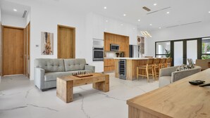 Un salon moderne avec un canapé gris, une table basse en bois et un coin cuisine doté de meubles en bois et d’un four à micro-ondes.