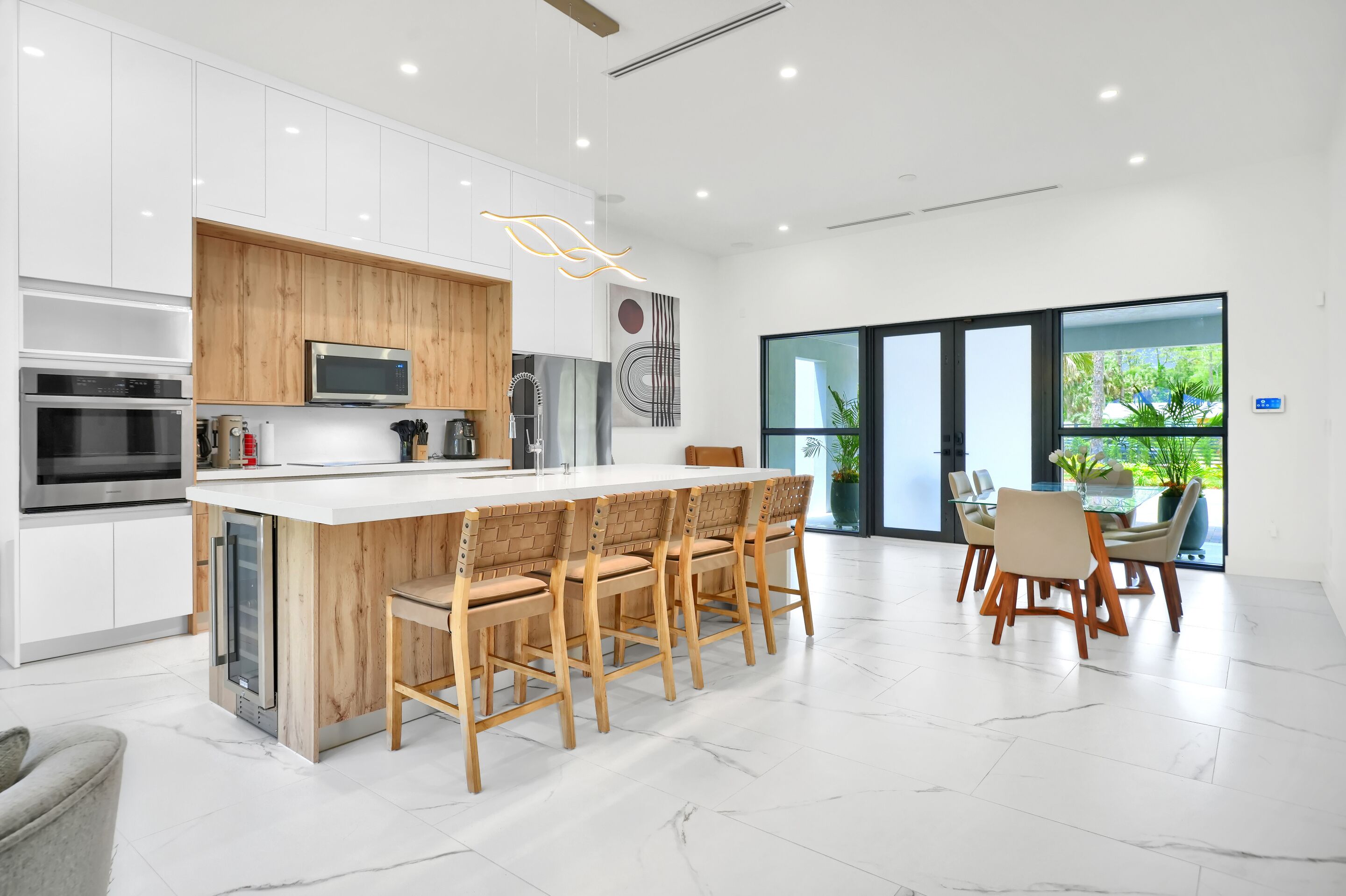 A modern kitchen with white cabinetry, a wooden island with bar stools, and a dining area with a glass table and chairs.
