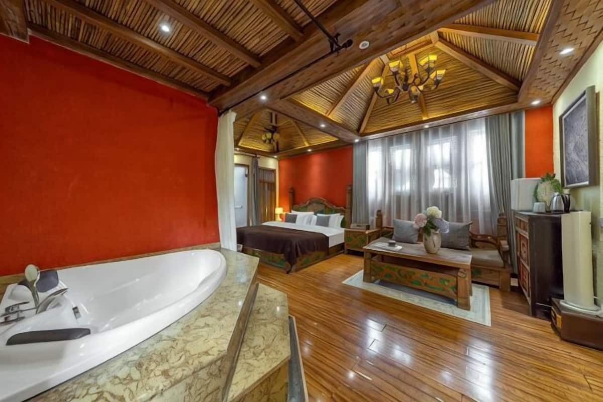 A spacious room with a large bathtub, a bed, a sofa, and a television.