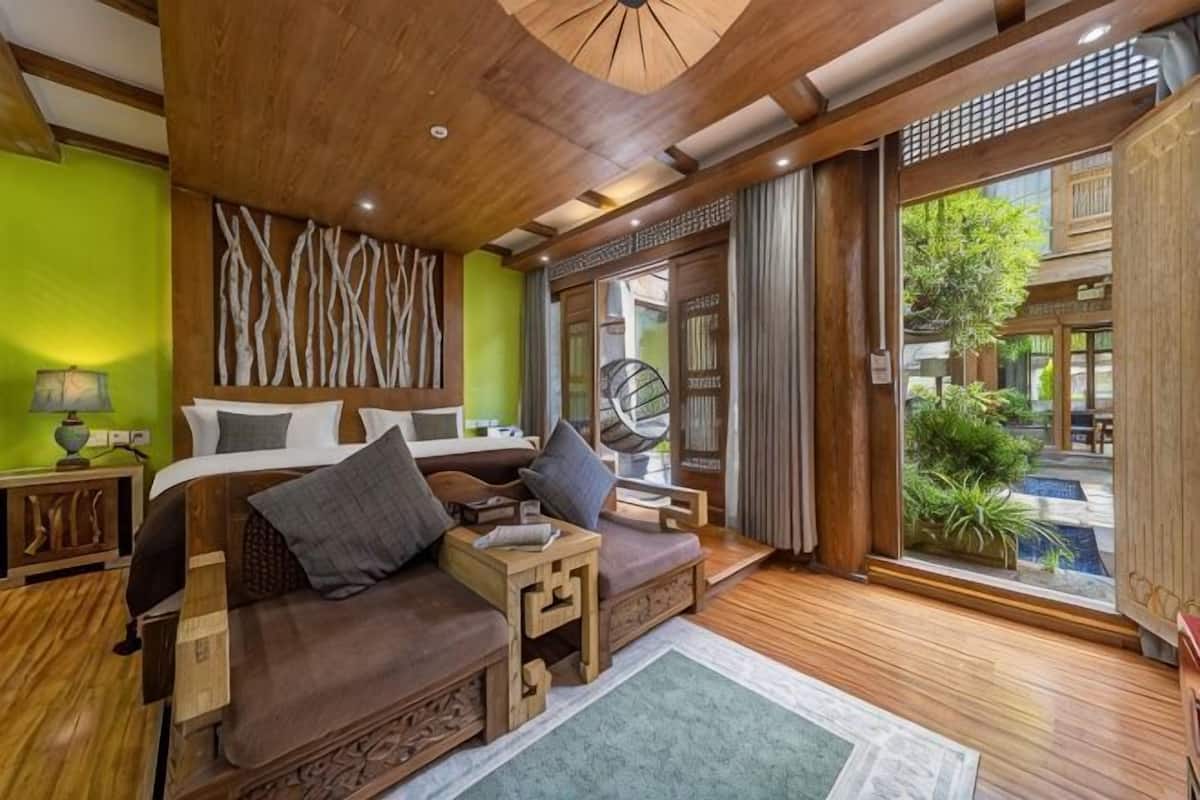 A room with a bed, a sofa, a small table, and a window with a view of a garden.