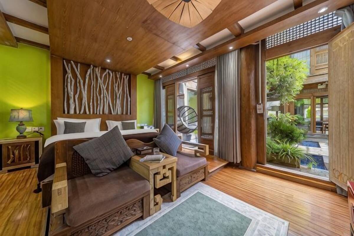 A room with a bed, a sofa, a small table, and a window with a view of a garden.