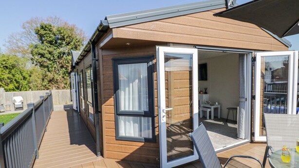 A wooden deck with a glass door leading to a room with a dining table and chairs. - Casa De Rhu (Evesham)