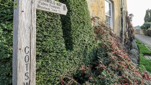 A wooden signpost with 'COTSWOLD WAY' and 'Broadway Tower' written on it, set against a backdrop of a building and lush greenery. - Casa De Rhu (Evesham)