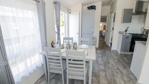 A compact kitchen with a dining area, featuring a wooden floor, white cabinetry, and a small dining table set for two. - Casa De Rhu (Evesham)