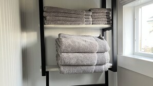 A bathroom with a towel rack holding folded towels, a toilet, and a window. - Charming Tiny House minutes from Syracuse! (Syracuse)