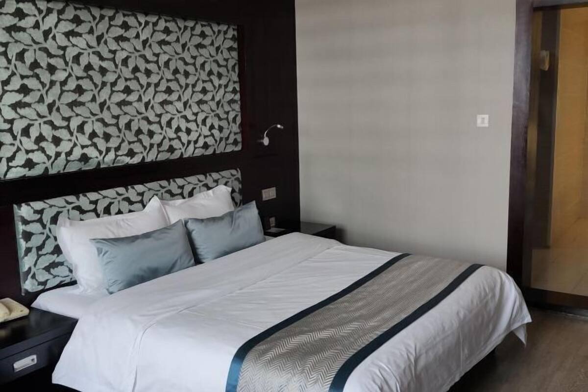 Een hotelkamer met een bed, een nachtkastje, een muur met een bladmotief en een deur.